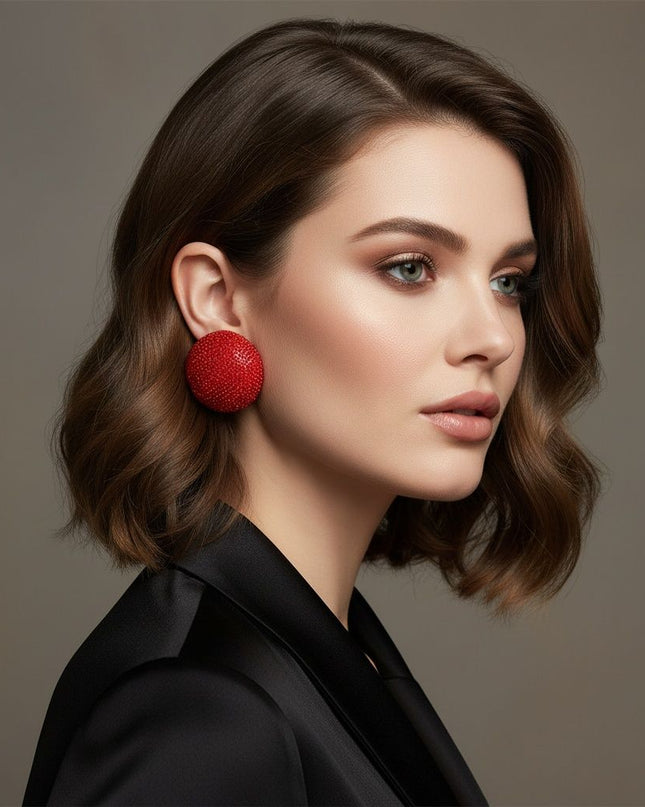 Women's Clip-On Earrings. Maximum Sparkle Statement Earrings. Bold Hollow Gold Metal Oversized Domed Clip-On Earrings Encrusted with Shimmering Red Rhinestones. Dome Measures .5 inches tall. Paddle Back Closure.