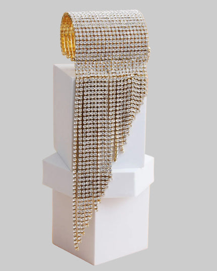 A bold gold cuff featuring twenty sleek fringe lines that drape with fluid, eye‑catching movement. Crafted from polished metal in a radiant gold finish, this adjustable statement piece delivers high‑impact shine with a modern, geometric edge. 