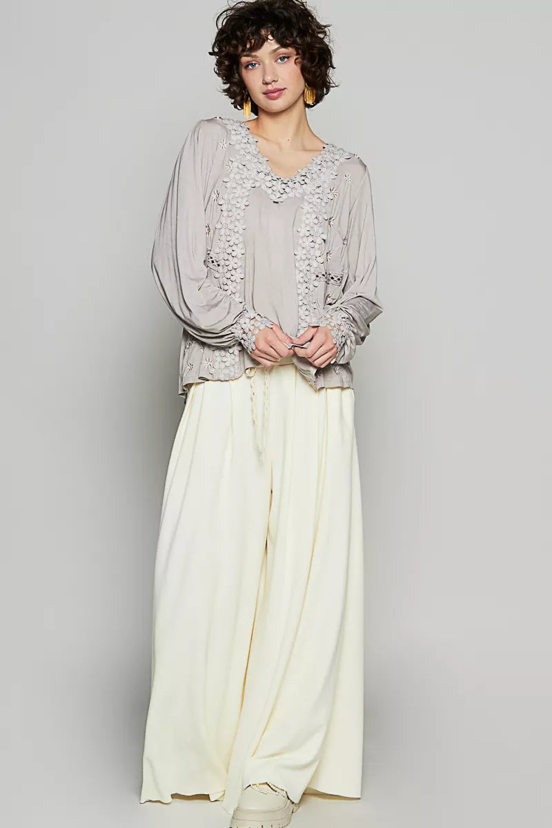 A light gray blouse with lace details and white pants