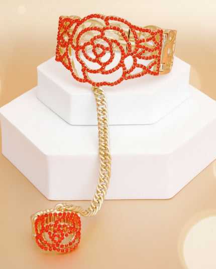 Women's Bracelet Hand Chain Gold Metal Rigid Cutout Rose Design Cuff Bracelet Featuring Red Rhinestone Detailing and Hinge Magnetic Closure. Also Features Textured Metal Hand Chain with Stretch Rose Ring. Chain measures 4" long. Ring Detail measures 1".