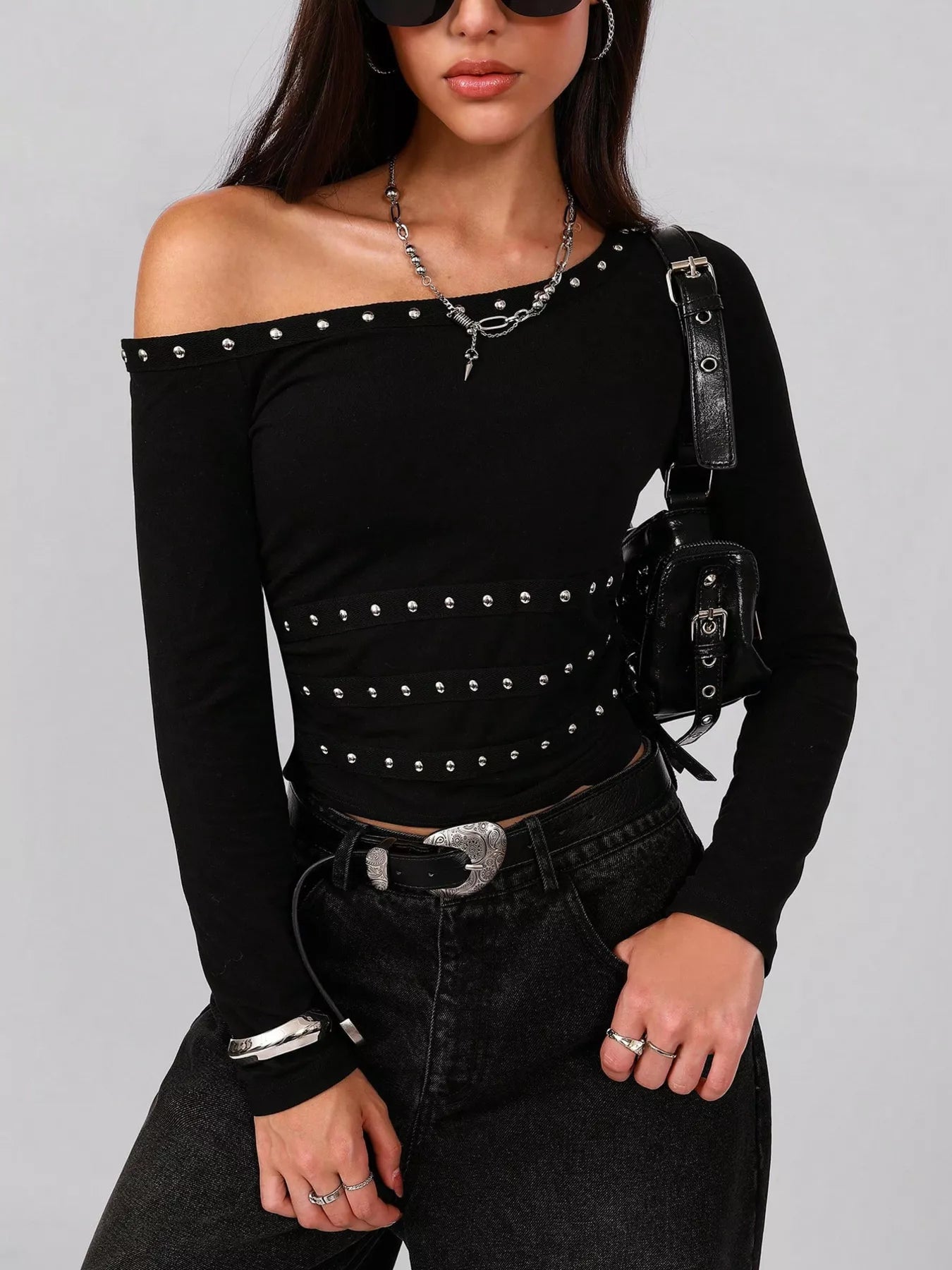 Black off-shoulder top with studs, paired with black pants.
