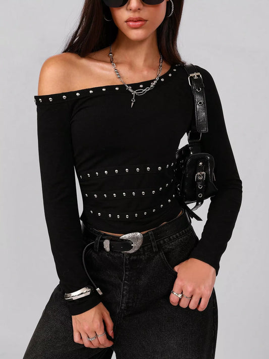 Black off-shoulder top with studs, paired with black pants.