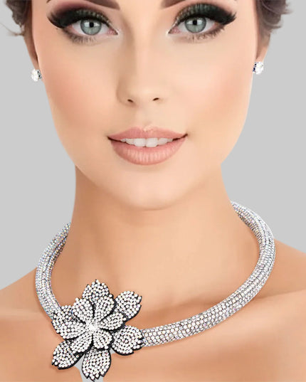 Women's Choker Necklace Set Bling Aurora Borealis Rhinestone Coated Rigid Tube Choker Featuring Elegant Layered Flower Rhinestone Offset Detail. Silver Metal Lobster Clasp Closure. Black Felt Backing on Flowers. Flower measures 2.5". Includes Matching Rhinestone Stud Post Earrings.
