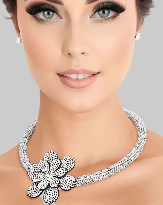 Women's Choker Necklace Set Bling Aurora Borealis Rhinestone Coated Rigid Tube Choker Featuring Elegant Layered Flower Rhinestone Offset Detail. Silver Metal Lobster Clasp Closure. Black Felt Backing on Flowers. Flower measures 2.5". Includes Matching Rhinestone Stud Post Earrings.
